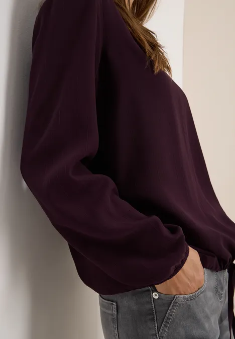 Frau mit dunkler Bluse und grauer Jeans steckt eine Hand in die Hosentasche.